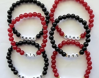 Puede incluir: Seis pulseras elásticas hechas de cuentas redondas negras y rojas. Cada pulsera presenta cuentas de letras blancas que forman las palabras ARMY, BTS o ARIRANG. Las cuentas de letras están acentuadas con pequeños espaciadores metálicos.