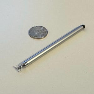 May include: A silver-coloured stylus featuring a clear circular disc tip at one end and a small black rubber tip at the other, placed beside a Canadian nickel coin to provide a sense of scale for the slender, cylindrical metal instrument.