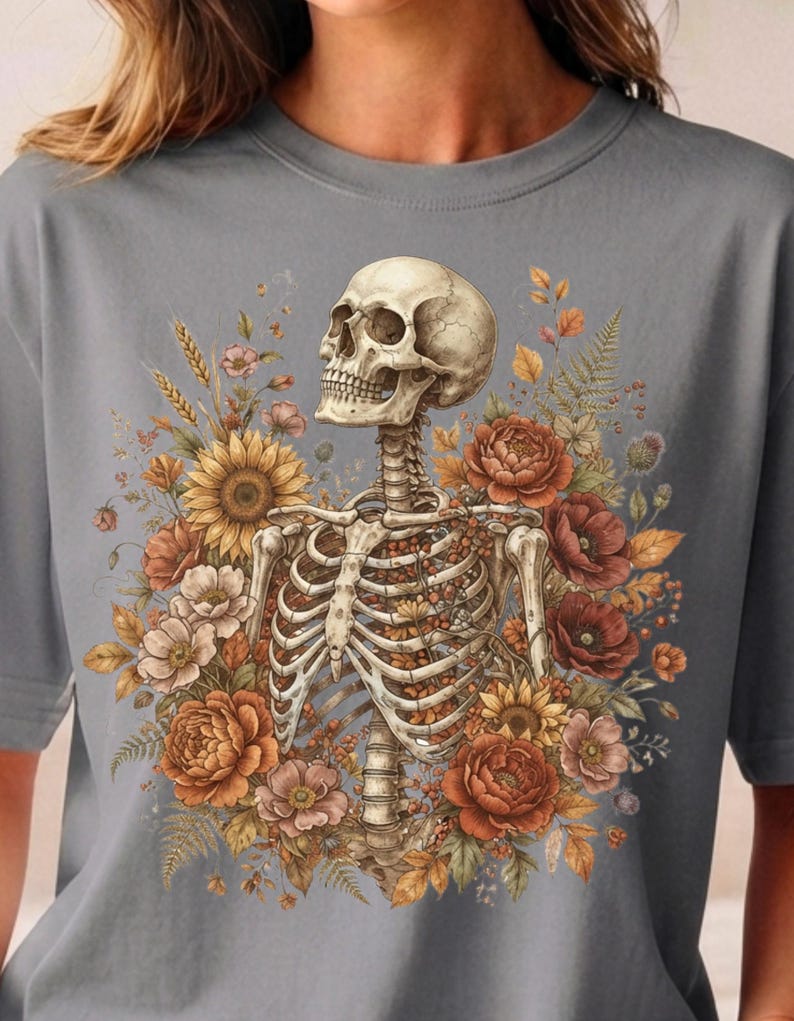 May include: A grey t-shirt featuring a graphic print of a human skeleton torso surrounded by a vibrant arrangement of autumn-toned flowers, including sunflowers, poppies, and peonies, with wheat stalks and fern leaves integrated into the design.