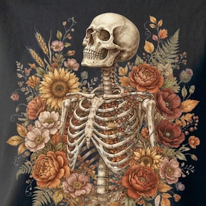 May include: A black t-shirt featuring a detailed graphic of a human skeleton torso and skull surrounded by a vibrant arrangement of autumn-toned flowers, including sunflowers, poppies, and ferns, with small berries nestled within the rib cage.