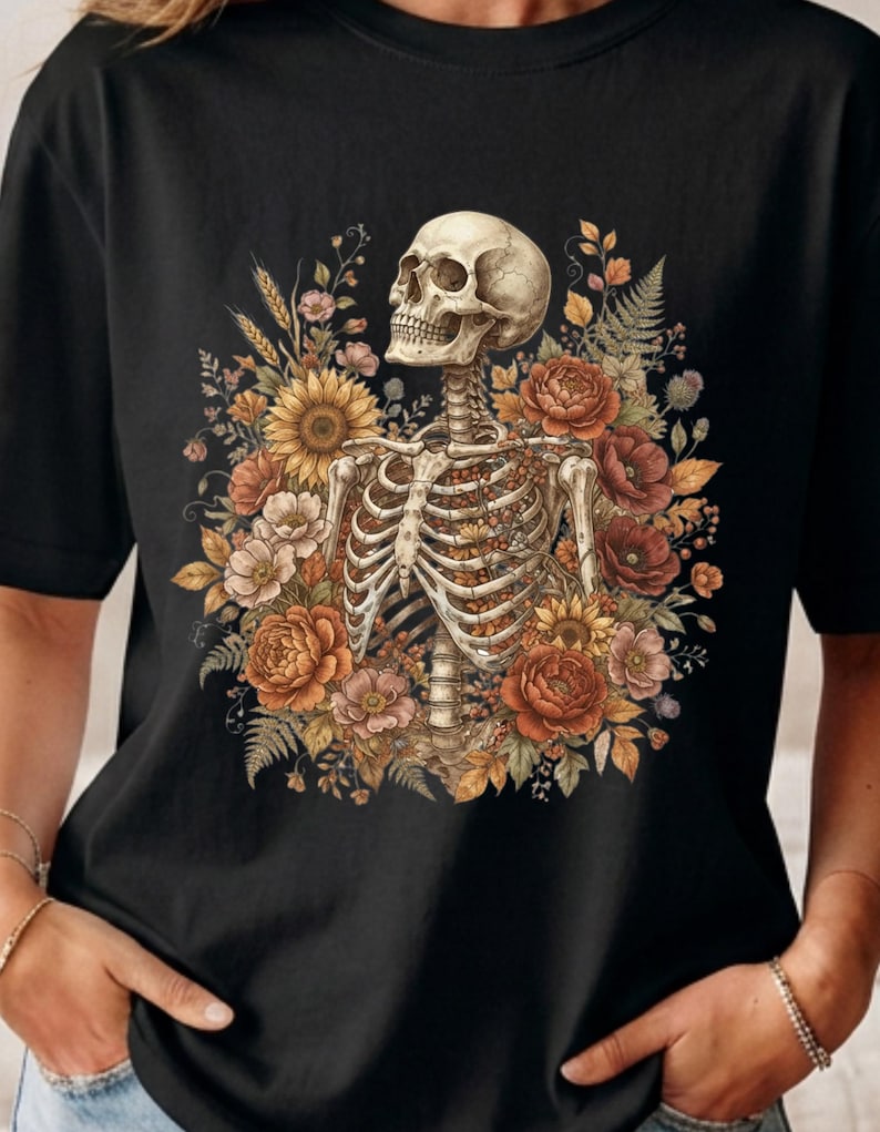 May include: A black t-shirt featuring a graphic print of a human skeleton torso surrounded by a vibrant arrangement of autumn-colored flowers, including sunflowers, poppies, and ferns, with the skeleton facing toward the upper left side.