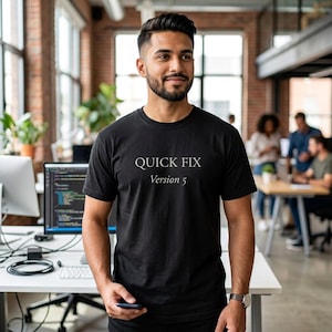 May include: A black short-sleeved t-shirt featuring the white text "QUICK FIX" on the top line and "Version 5" on the line below. The shirt has a crew neckline and a standard fit, constructed from a solid black fabric with clear, centred lettering.