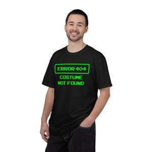 Puede incluir: Una camiseta negra de manga corta con texto pixelado en verde brillante que dice ERROR 404 dentro de un borde rectangular, seguido del texto COSTUME NOT FOUND debajo. La camiseta tiene cuello redondo y un ajuste estándar.