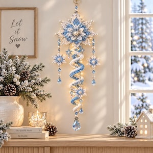 May include: A decorative hanging ornament featuring a large, intricate snowflake design in shades of white and blue, accented with beads and crystals. A spiral tail extends downward, adorned with smaller snowflake motifs and a clear teardrop crystal.