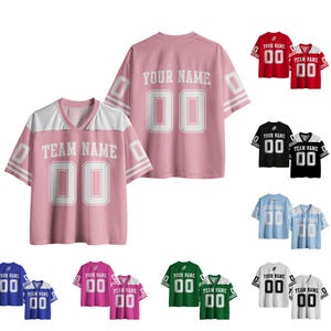 Puede incluir: Una colección de camisetas de manga corta con cuello en V en varios colores, incluyendo rosa, rojo, negro, azul claro, azul real, magenta, verde y blanco. Cada camiseta presenta el texto "TEAM NAME" y el número "00" en una fuente atlética.