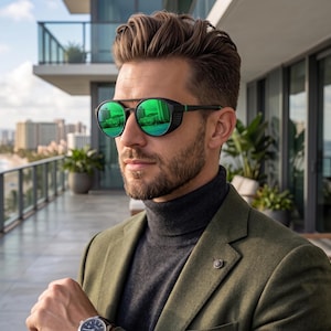 May include: Round sunglasses with black frames and reflective green lenses featuring side shields, worn with a dark gray turtleneck sweater, an olive green blazer with a lapel pin, and a wristwatch with a dark face and a leather strap.