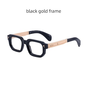 Può includere: Occhiali con montatura nera e aste color oro. La parte anteriore della montatura presenta piccole icone a forma di martello sugli angoli esterni. Le aste dorate sono decorate con un motivo a freccia. Il testo "black gold frame" appare sopra.