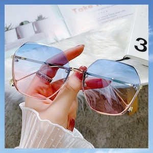 May include: Rimless sunglasses featuring a geometric, multi-faceted lens shape with a blue-to-pink gradient tint. The frames are constructed from thin, polished gold-tone metal, including a straight bridge and slender temples.