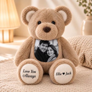 May include: A light brown plush teddy bear featuring a circular black and white photograph of a couple on its chest. The bear has cream-colored inner ears and foot pads. The left foot pad displays the text Love You Always and the right foot pad displays the text Ellie Heart Jack in a black serif font.