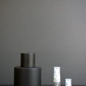 May include: A matte black cylindrical perfume bottle labeled Tom Ford Ombré Leather, accompanied by two clear glass spray vials. One vial is labeled 5ml sample and the other is labeled 2ml sample, both featuring white spray nozzles and clear plastic caps.