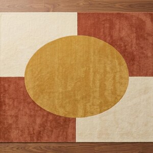 May include: A square area rug featuring a geometric design with four quadrants in alternating cream and terracotta colours. A large, solid mustard yellow oval shape is centred across the middle of the rug, overlapping the four quadrants.