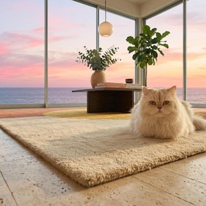 May include: A rectangular area rug featuring a geometric pattern in shades of cream, yellow, and terracotta. The rug has a textured, plush pile surface and is positioned on a light-coloured stone floor, providing a soft base for a long-haired cat.