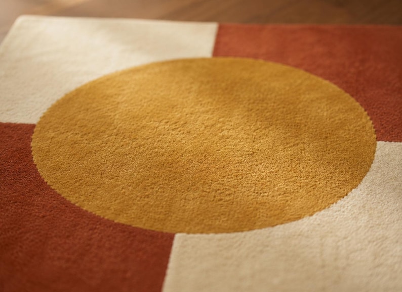 May include: A square rug featuring a large, centred mustard yellow circle set against a background of alternating cream and terracotta red geometric blocks. The rug has a dense, textured pile surface with clean, sharp edges between the colours.