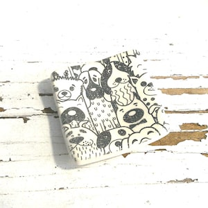 May include: A square ceramic tile featuring a black and white graphic print of various dog faces and patterns. The design includes multiple canine illustrations with different expressions, ears, and markings, all arranged in a dense, repeating pattern.