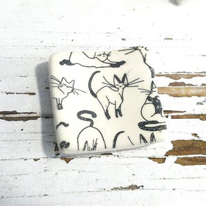 May include: A square ceramic tile featuring a repeating black line art pattern of various cats in different poses on a white background. The cats are depicted with simple strokes, showing silhouettes, sitting positions, and stretching movements.