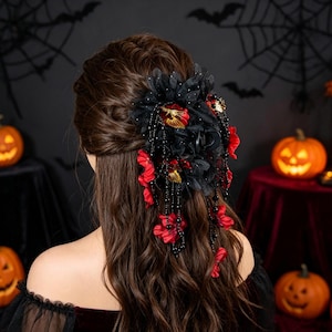 Pode incluir: Um acessório de cabelo com flores de tecido pretas e vermelhas, detalhes em tom dourado e fios de contas pretas pendentes. A peça está presa a uma presilha e posicionada em cabelos castanhos longos, criando um arranjo floral e de contas.