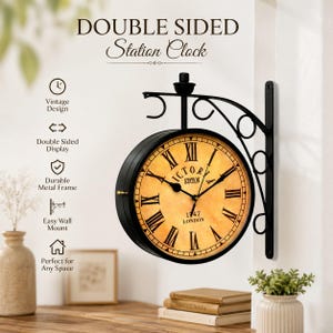 May include: A black double-sided station clock with a metal frame and a beige face featuring Roman numerals. The clock face displays the text Victoria Station 1747 London. It is mounted on a decorative black metal wall bracket with scrollwork.
