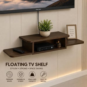 May include: A dark brown wooden floating TV shelf mounted on a wall. The shelf features a central enclosed compartment containing a black electronic device, with open side extensions holding a remote control, a potted green plant, and a small picture frame.