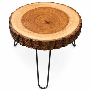May include: A round side table featuring a natural wood slice tabletop with visible grain patterns and a rough, textured bark edge. The tabletop is supported by three thin, black metal hairpin legs that extend downwards from the underside.