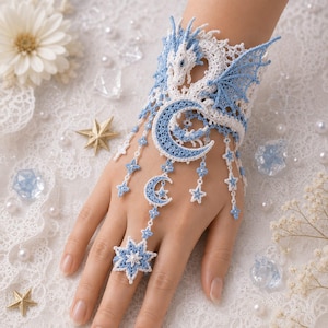 May include: A white and light blue lace hand ornament featuring a dragon motif on the wrist cuff, connected by delicate chains of small stars and crescent moons to a matching star-shaped ring that fits around the middle finger.