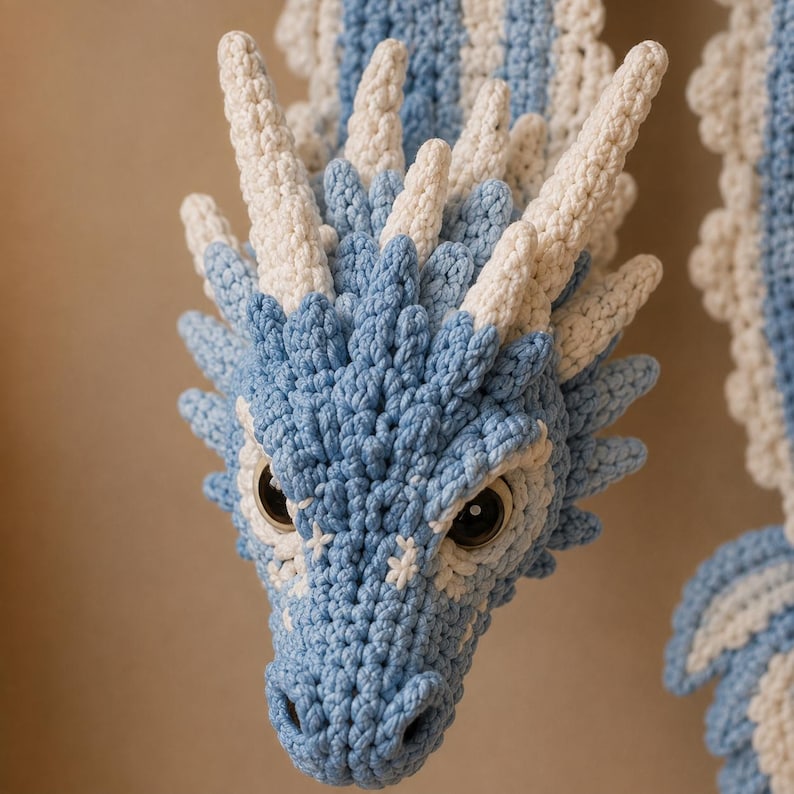 May include: A handcrafted crochet dragon head featuring light blue and cream yarn. The creature has prominent pointed horns, textured scales, and large dark inset eyes. The intricate stitching creates a detailed, layered appearance across the snout.