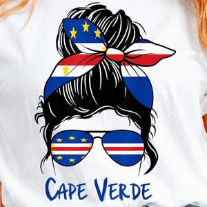 May include: A white t-shirt featuring a graphic of a messy bun hairstyle with a headband patterned after the Cape Verde flag. The graphic includes aviator sunglasses with the Cape Verde flag design on the lenses and the text CAPE VERDE below.