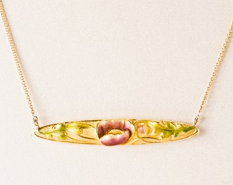 May include: A gold chain necklace with a delicate pendant featuring a pink flower with green leaves. The pendant is shaped like a long oval.