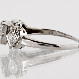 Puede incluir: Un anillo de compromiso vintage de oro blanco de 18 quilates con un diamante central de forma cuadrada y diamantes m&aacute;s peque&ntilde;os en la banda. El anillo tiene un dise&ntilde;o delicado e intrincado.