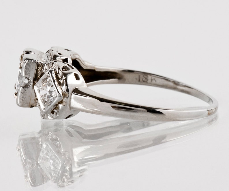 Puede incluir: Un anillo de compromiso vintage de oro blanco de 18 quilates con un diamante central de forma cuadrada y diamantes m&aacute;s peque&ntilde;os en la banda. El anillo tiene un dise&ntilde;o delicado e intrincado.
