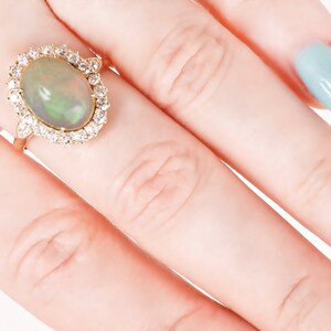 May include: A gold ring with a large oval opal gemstone surrounded by a halo of smaller diamonds.