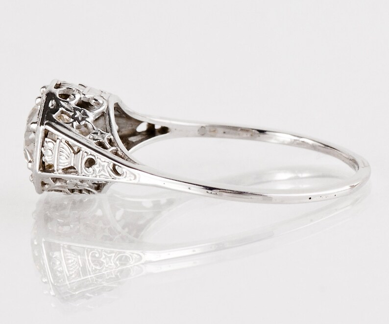 K&ouml;nnte beinhalten: Ein silberner Ring mit einem filigranen Design und einem runden, klaren Edelstein in der Mitte.