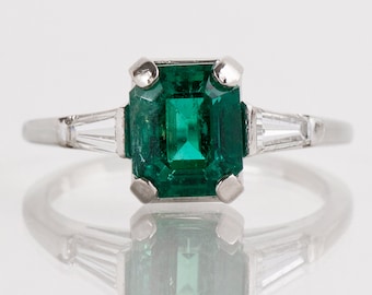 May include: A platinum ring with a large emerald-cut green gemstone and two smaller baguette-cut diamonds on either side.