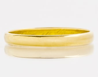 May include: A simple gold wedding band. The band is smooth and polished, with a slightly rounded edge.