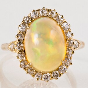May include: A gold ring with a large oval opal gemstone surrounded by a halo of smaller diamonds.