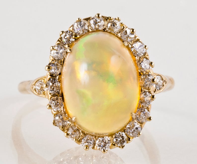 May include: A gold ring with a large oval opal gemstone surrounded by a halo of smaller diamonds.