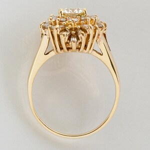 May include: A gold ring featuring a cluster of diamonds. The central diamond is surrounded by smaller stones, creating a floral or starburst design. The band is a simple, polished gold.