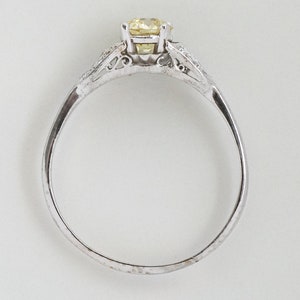 May include: A silver ring with a round, yellow gemstone as the centerpiece. The ring has a delicate design with smaller, clear stones on either side of the main stone. The band is thin and polished, creating a classic and elegant look.