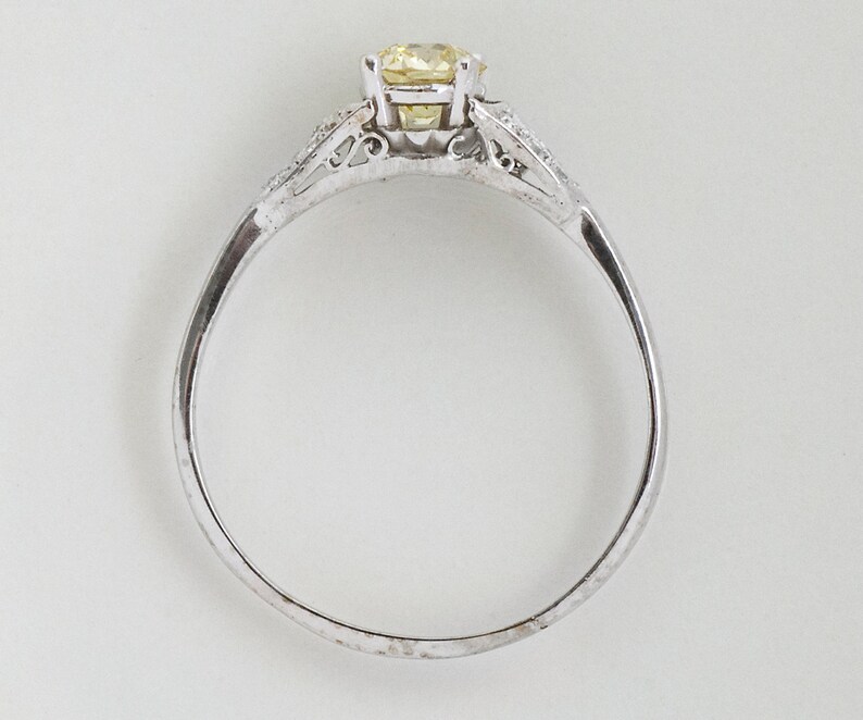 May include: A silver ring with a round, yellow gemstone as the centerpiece. The ring has a delicate design with smaller, clear stones on either side of the main stone. The band is thin and polished, creating a classic and elegant look.