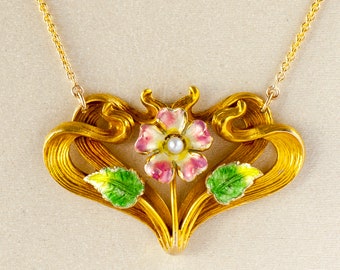 May include: Gold-toned necklace featuring a floral pendant with a pearl center and pink and white enamel petals. The pendant has a stylized, flowing design with green enamel leaves and is suspended from a delicate chain.