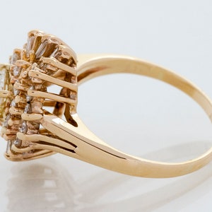 May include: A gold ring featuring a cluster of diamonds. The ring has a central, oval-cut diamond surrounded by smaller, baguette-cut diamonds, creating a floral or starburst design. The band is a simple, polished gold.