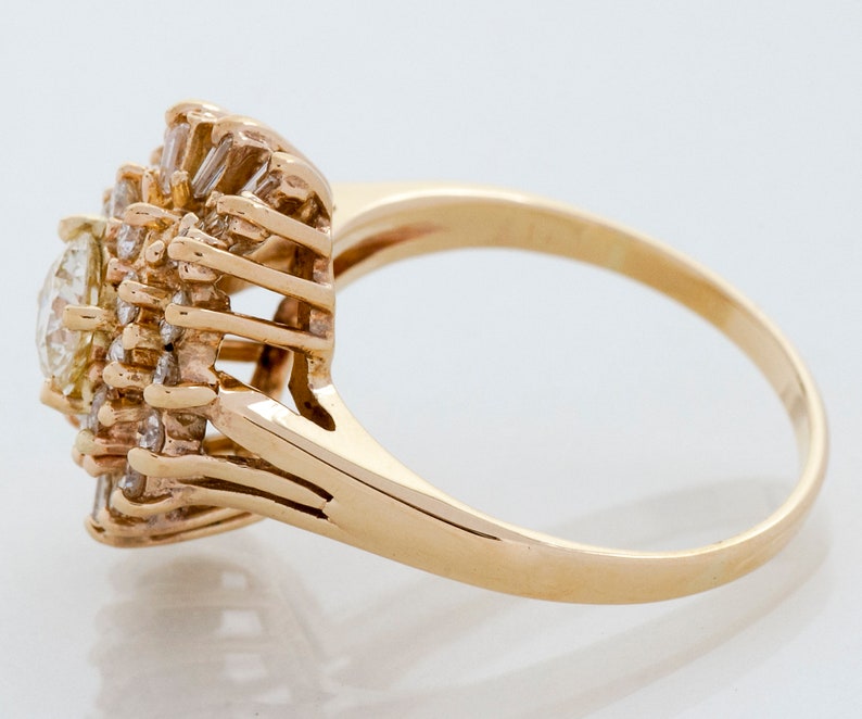 May include: A gold ring featuring a cluster of diamonds. The ring has a central, oval-cut diamond surrounded by smaller, baguette-cut diamonds, creating a floral or starburst design. The band is a simple, polished gold.