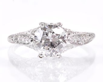 May include: A platinum engagement ring with a large, round, brilliant-cut diamond center stone and smaller diamonds set in a delicate, intricate design along the band.