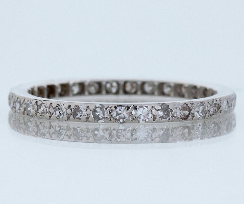 May include: A thin silver band with a row of small diamonds set in a continuous line around the entire band.