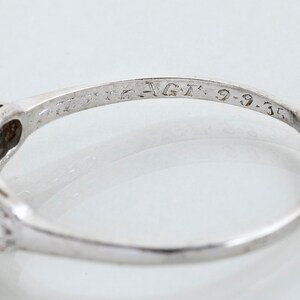 May include: Close-up of a silver ring with a filigree design and small gemstones. The ring is engraved with the text "AGT: 9-9-35". The ring is set against a white background.