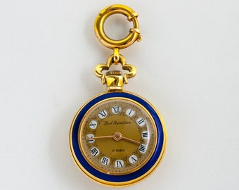 Puede incluir: Un reloj de bolsillo dorado con un bisel de esmalte azul y una esfera dorada. El reloj presenta números romanos y el texto "Paul Byantier" y "17 Rubis". Tiene una parte superior decorativa y un cierre.