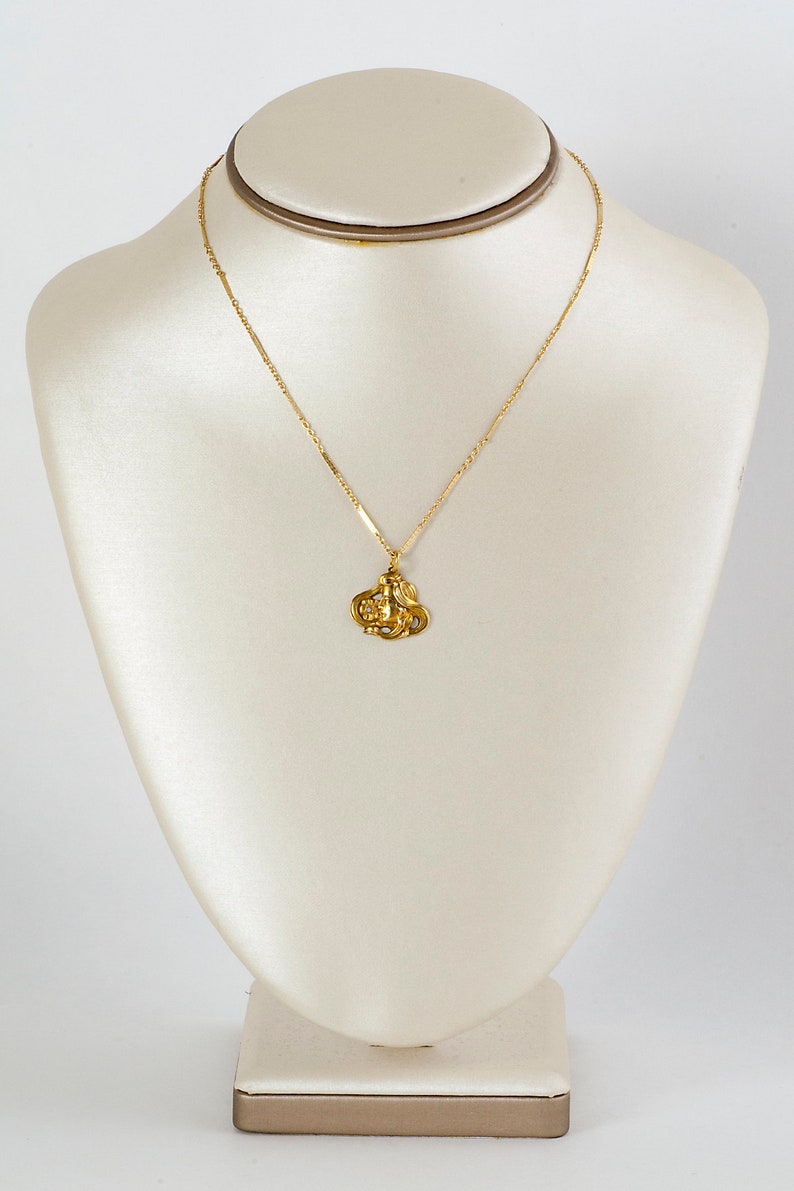 May include: A gold chain necklace with a pendant featuring a detailed design of a woman's face.