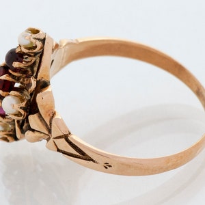 Puede incluir: Un anillo de oro con un grupo de piedras preciosas. El centro del anillo presenta una combinaci&oacute;n de piedras rojas, rosas y blancas, probablemente granates, rub&iacute;es y perlas. La banda tiene un intrincado dise&ntilde;o floral.