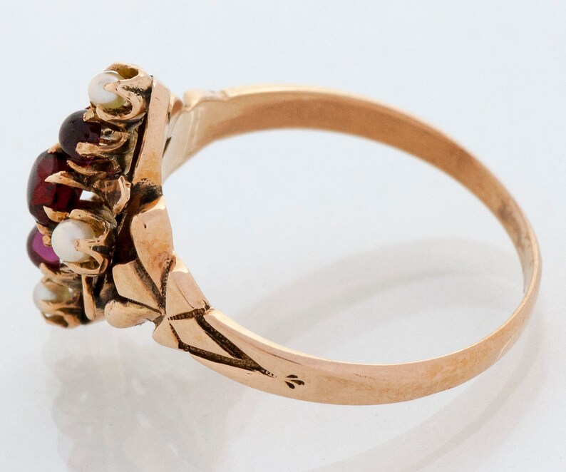 Puede incluir: Un anillo de oro con un grupo de piedras preciosas. El centro del anillo presenta una combinaci&oacute;n de piedras rojas, rosas y blancas, probablemente granates, rub&iacute;es y perlas. La banda tiene un intrincado dise&ntilde;o floral.