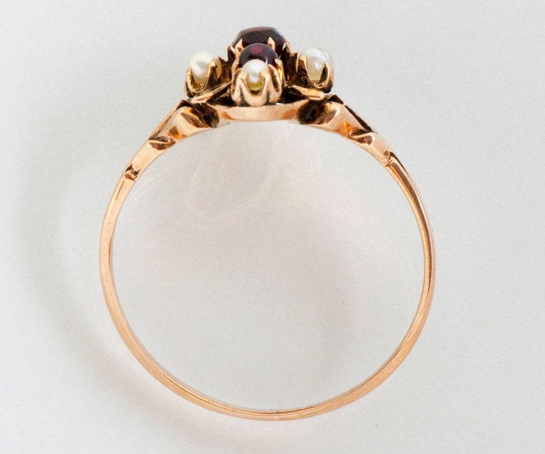 Puede incluir: Anillo de oro con una piedra roja ovalada central, flanqueada por tres peque&ntilde;as perlas blancas redondas. La banda del anillo es de oro pulido y el engaste tiene detalles intrincados. Joya cl&aacute;sica.