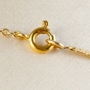 May include: Close-up of a gold chain necklace clasp. The clasp is a round, spring-loaded ring with a small, decorative piece on top.